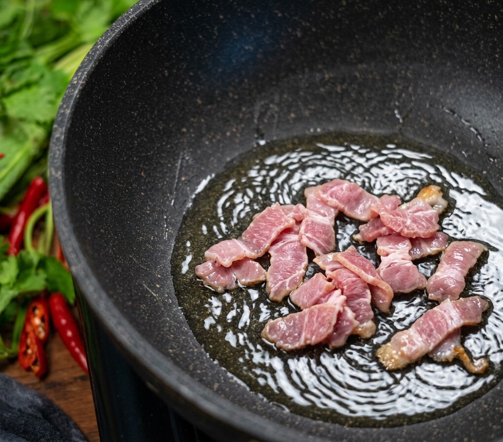 Morceaux de bacon coupés qui grésillent dans une poêle antiadhésive sombre, la graisse formant des bulles pendant que la viande dore.