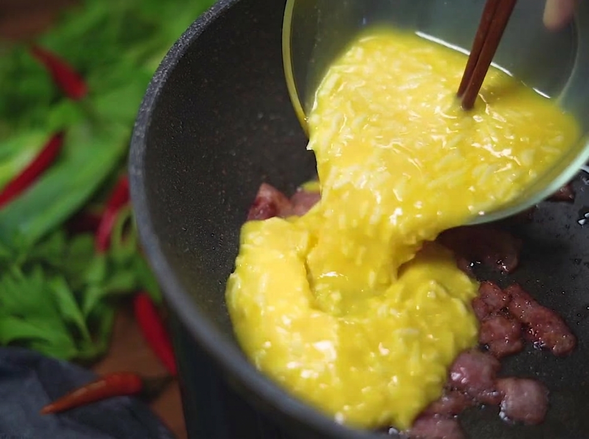 Le mélange dœufs et de fromage versé dun bol en verre dans une poêle chaude contenant les morceaux de bacon croustillants.
