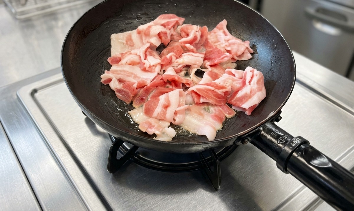 Tranches de poitrine de porc en train de cuire dans une poêle noire sur une cuisinière en acier inoxydable.