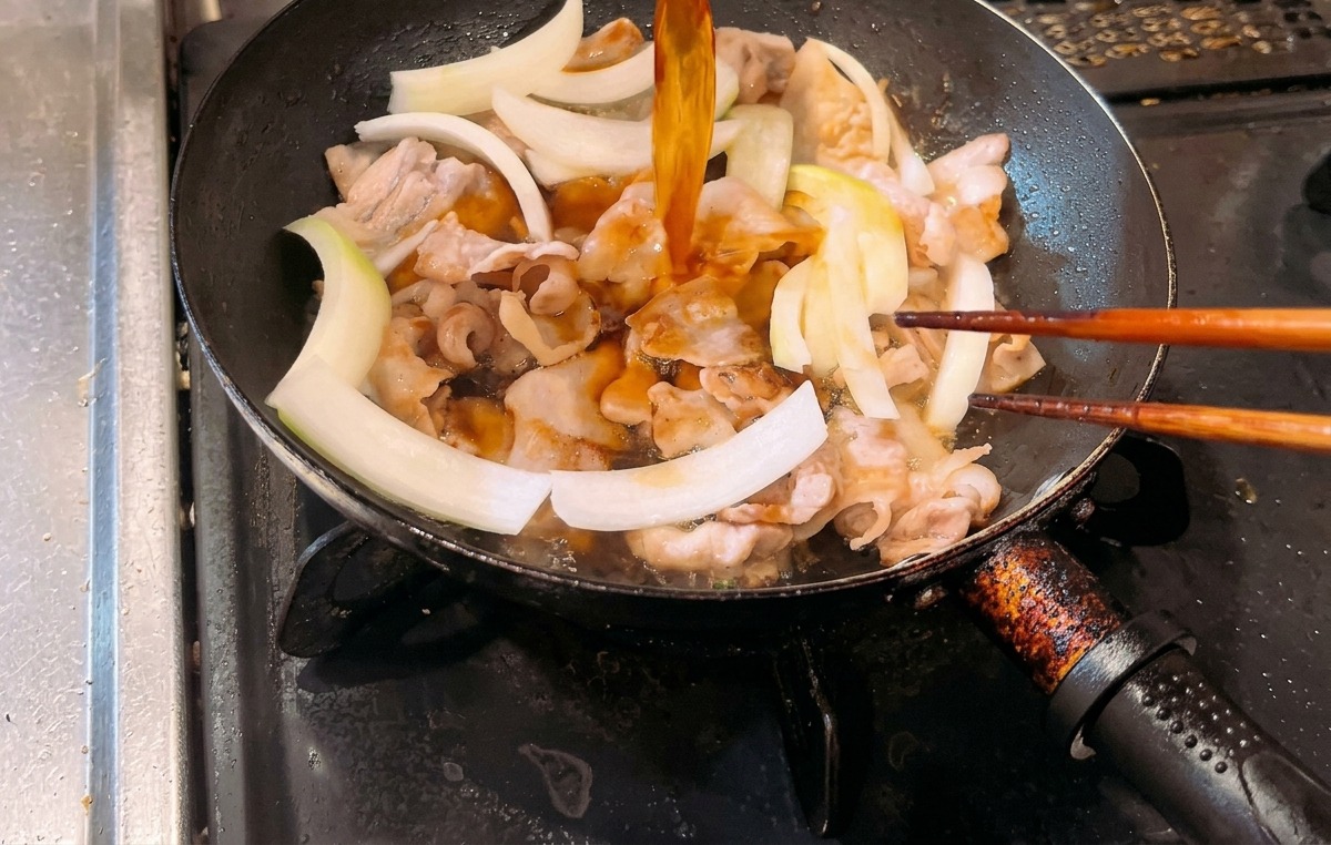 Versement dune sauce de couleur ambrée dans une poêle contenant la poitrine de porc cuite et des lamelles doignon blanc cru.