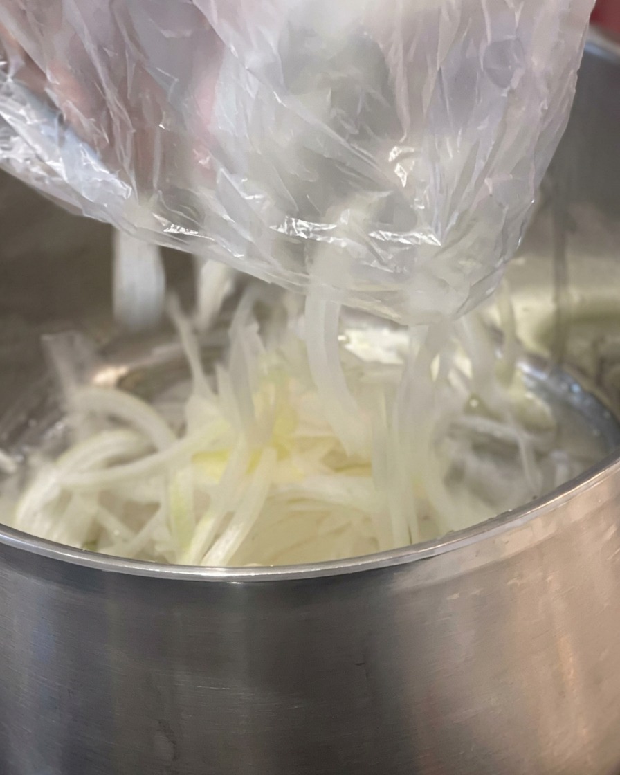 Des lamelles doignon blanc versées dans une casserole en acier inoxydable contenant un morceau de beurre jaune.
