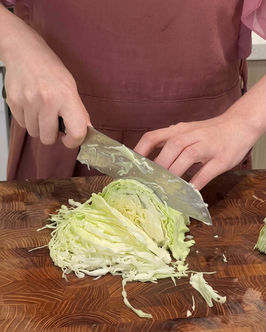 Gros plan dun chef éminçant finement un chou vert en fines lanières sur une planche à découper en bois avec un grand couteau.
