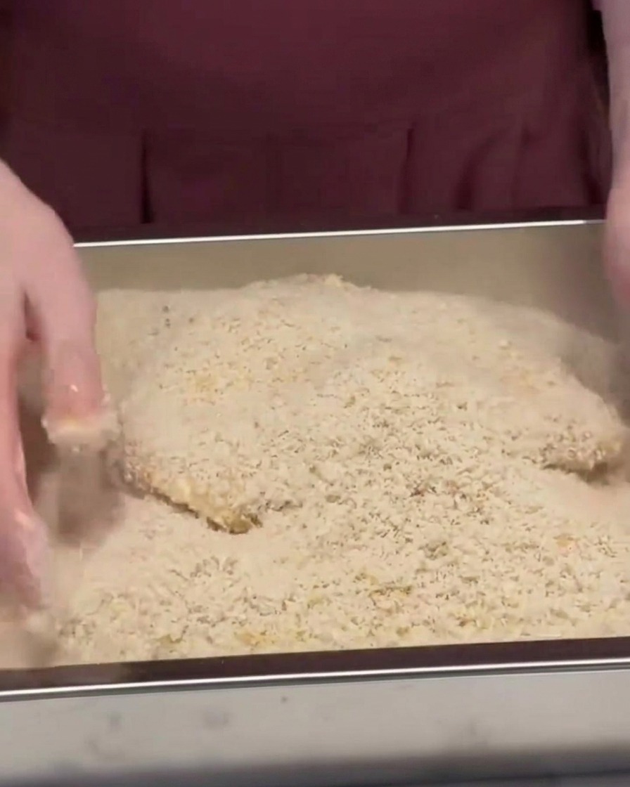 Une escalope de porc recouverte et pressée dans un plateau métallique rempli de chapelure panko.