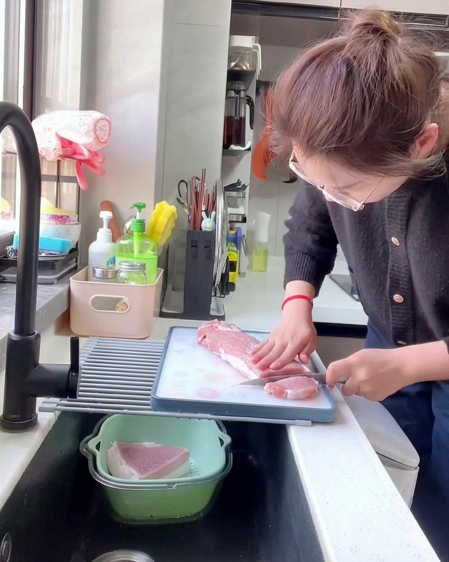 Une personne coupant une longe de porc crue en tranches épaisses de 1 cm sur une planche à découper blanche.