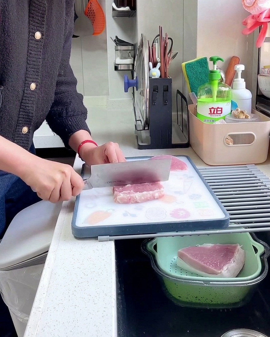 Une main tenant un grand couperet en métal et utilisant le dos de la blade pour battre et attendrir une tranche de porc crue.