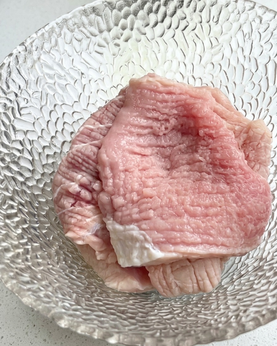Gros plan sur un bol en verre contenant des tranches de porc crues garnies doignons verts émincés et dassaisonnements liquides.