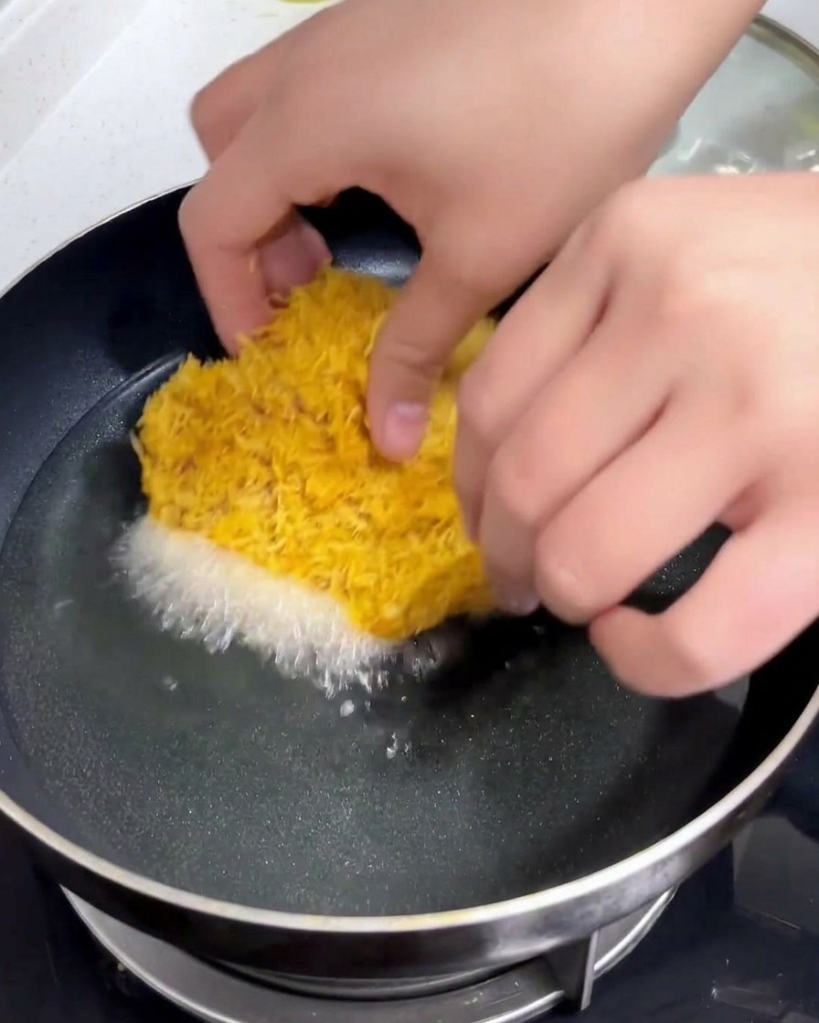 Une escalope de porc panée délicatement déposée à la main dans une poêle remplie dhuile chaude et miroitante.