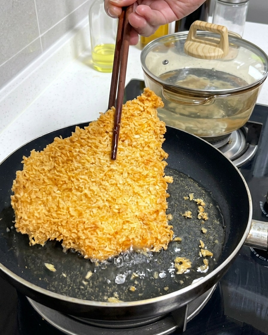 Une grande escalope de porc panée, croustillante et dorée, retournée avec des baguettes en bois dans une poêle peu profonde remplie dhuile bouillonnante.