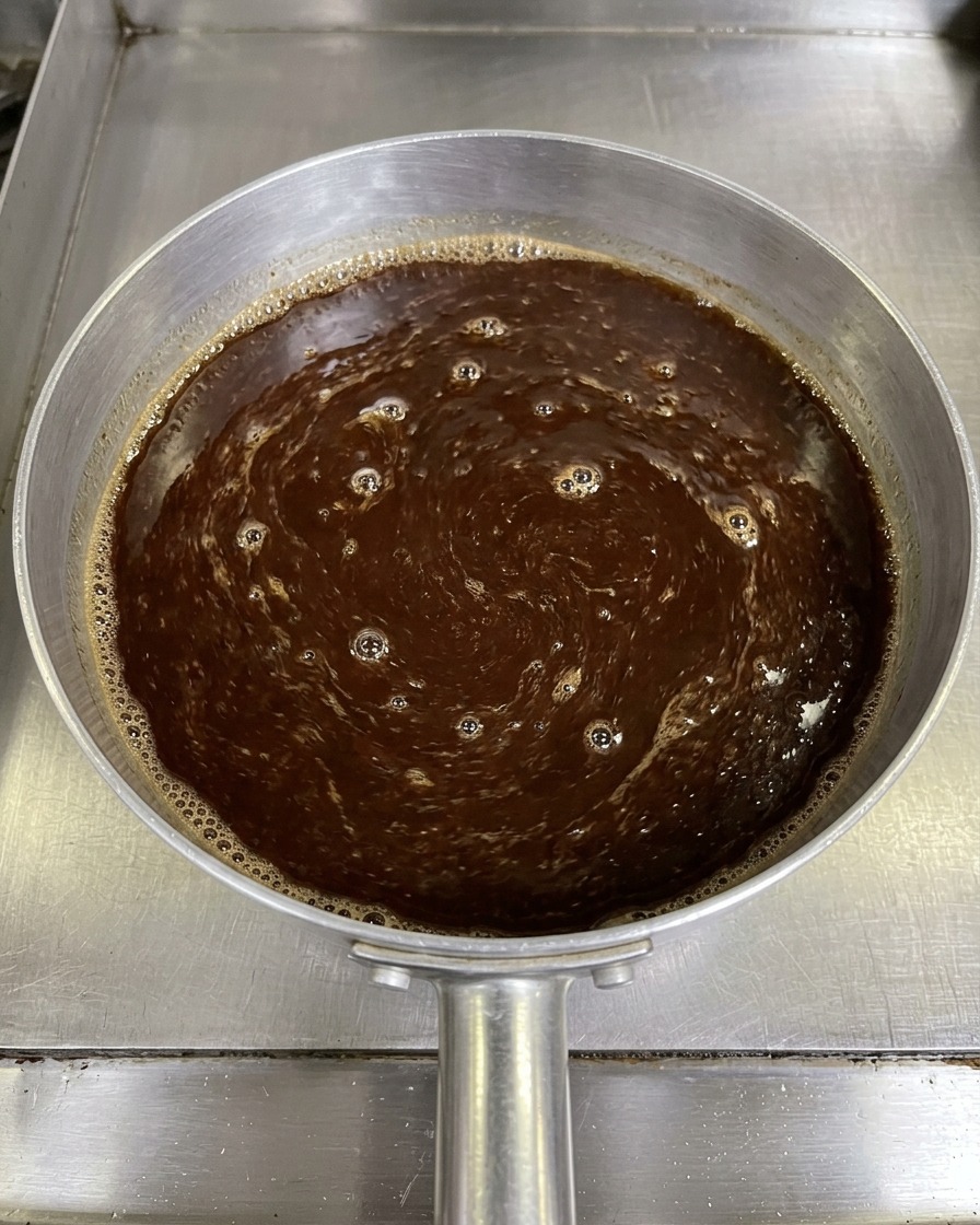 Vue de dessus dun mélange de sauce miso marron foncé remué avec une paire de baguettes dans une petite casserole en aluminium.