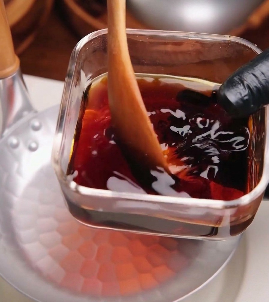 De la sauce foncée pour katsudon versée depuis un récipient en verre dans une poêle en métal martelé peu profonde.