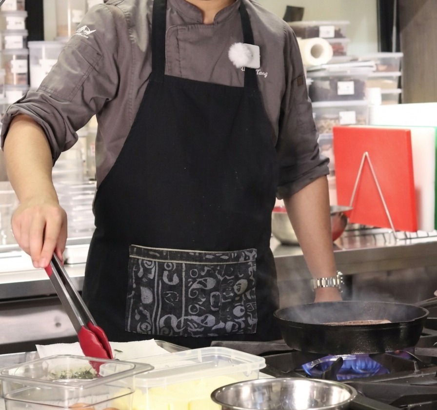Le chef utilisant une pince pour transférer des brins de thym frais et de lail dun récipient vers la poêle.