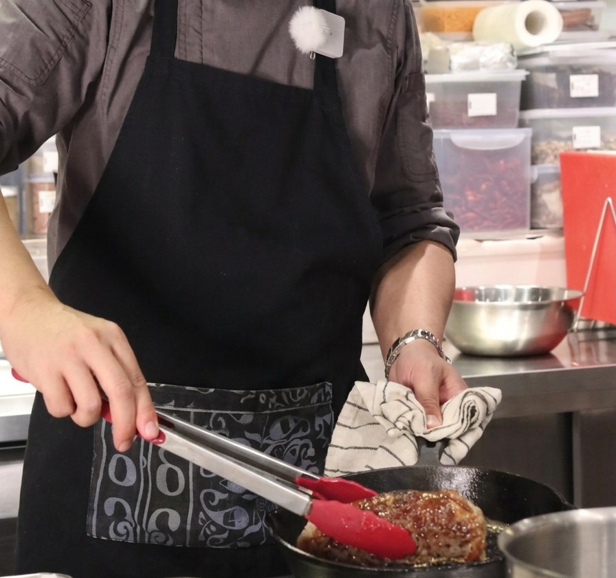 Gros plan dun gros morceau de bœuf maintenu verticalement avec une pince à embouts rouges dans une poêle en fonte chaude.