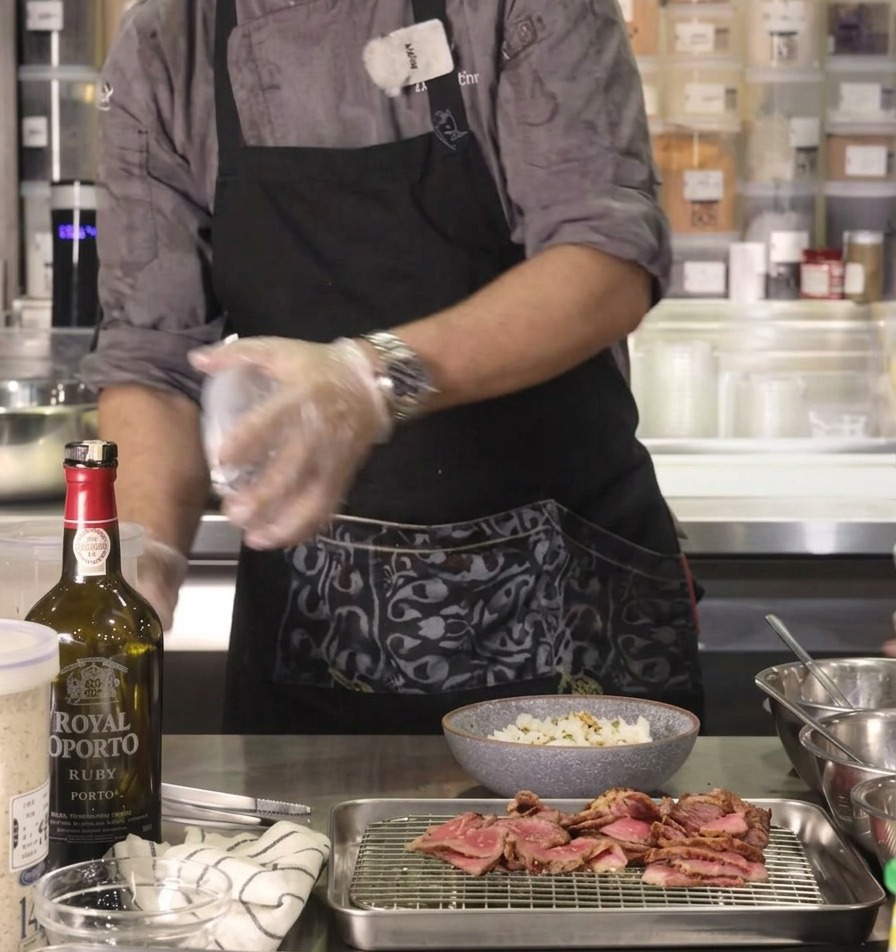 La main du chef secouant de lassaisonnement furikake savoureux sur un bol de riz posé sur un plan de travail en acier inoxydable.