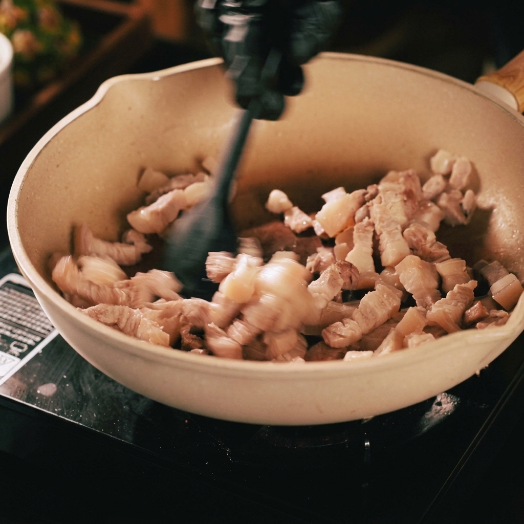 Lanières de porc sautées dans une poêle beige avec une spatule noire, montrant la viande dorée et la graisse fondue.