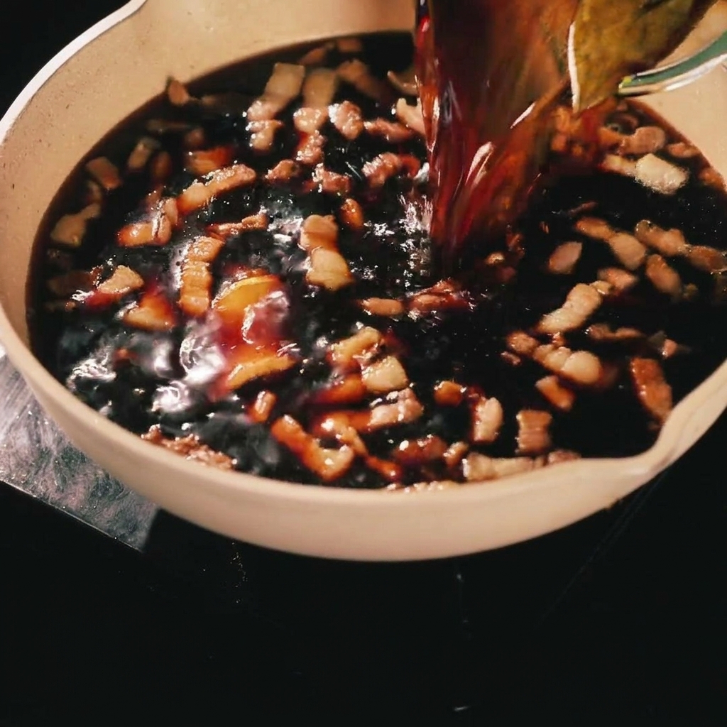 Une marinade brune et savoureuse versée depuis un récipient en verre sur les lanières de porc dorées dans une poêle de cuisson.