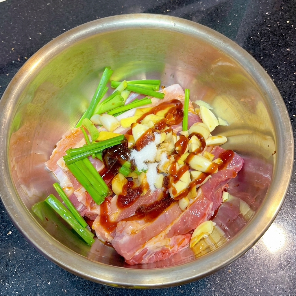 Un petit tas de sel blanc et de poudre dépices brun-rouge posé sur des tranches de porc marinées et des aromates dans un bol en métal.
