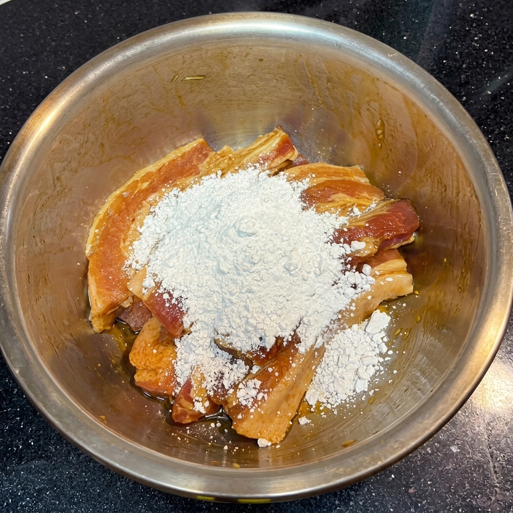 Un grand monticule de fécule de patate douce blanche et poudreuse posé sur des tranches de porc marinées brun foncé dans un bol.