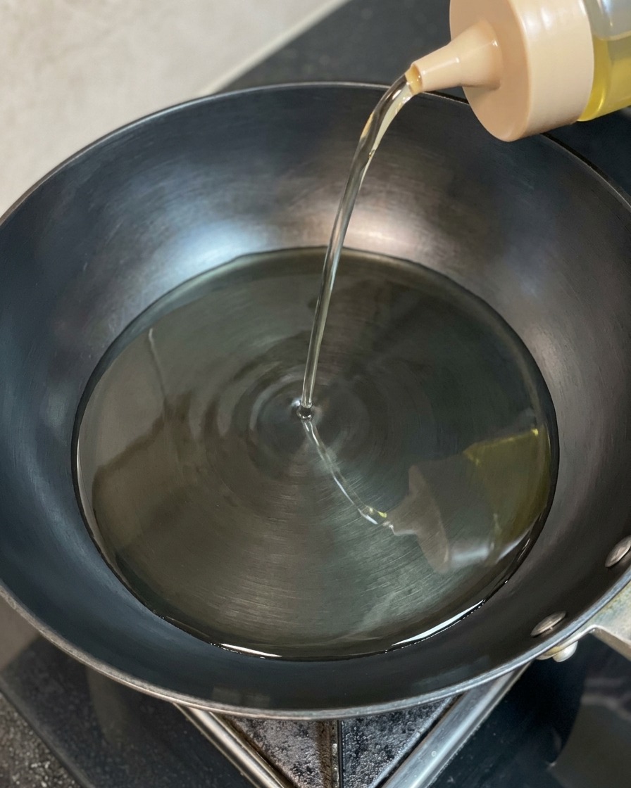 Huile de cuisson claire versée depuis une bouteille souple dans un wok sombre et chauffé.