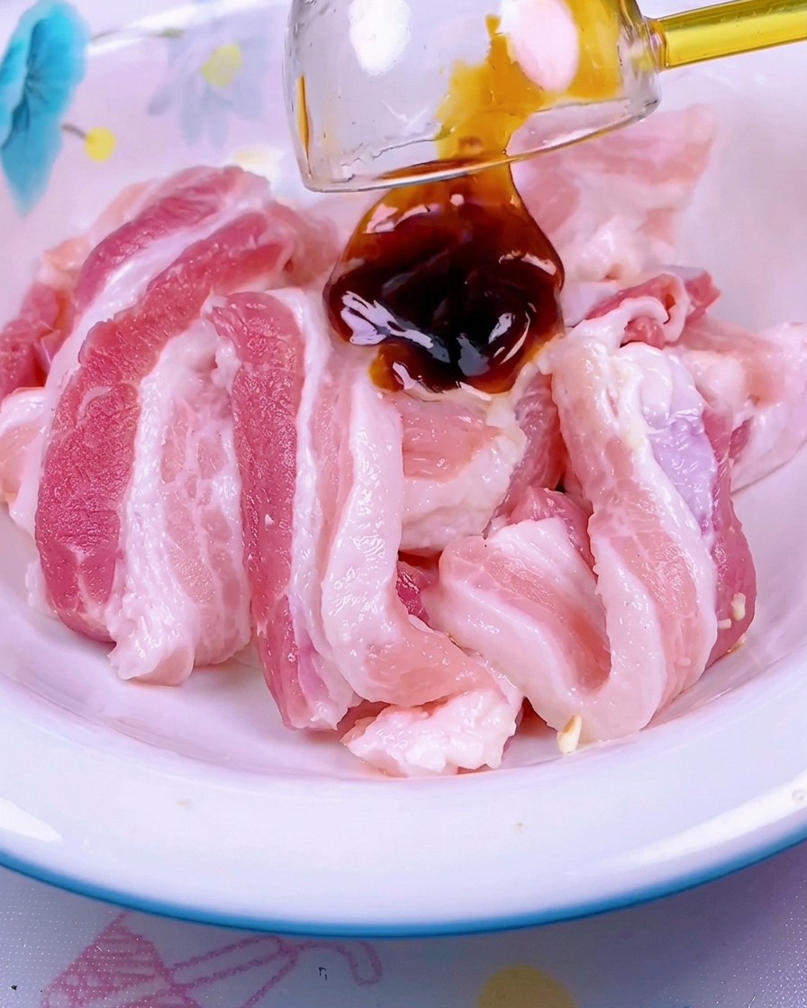 Sauce rouge foncé versée sur un tas de poitrine de porc crue en tranches dans un bol en céramique blanche.