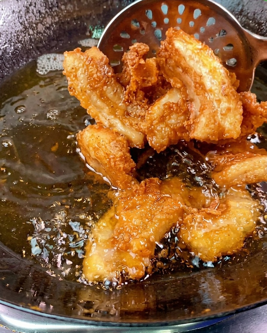 Tranches de poitrine de porc croustillantes et dorées retirées dun wok dhuile bouillonnante à laide dune écumoire métallique.