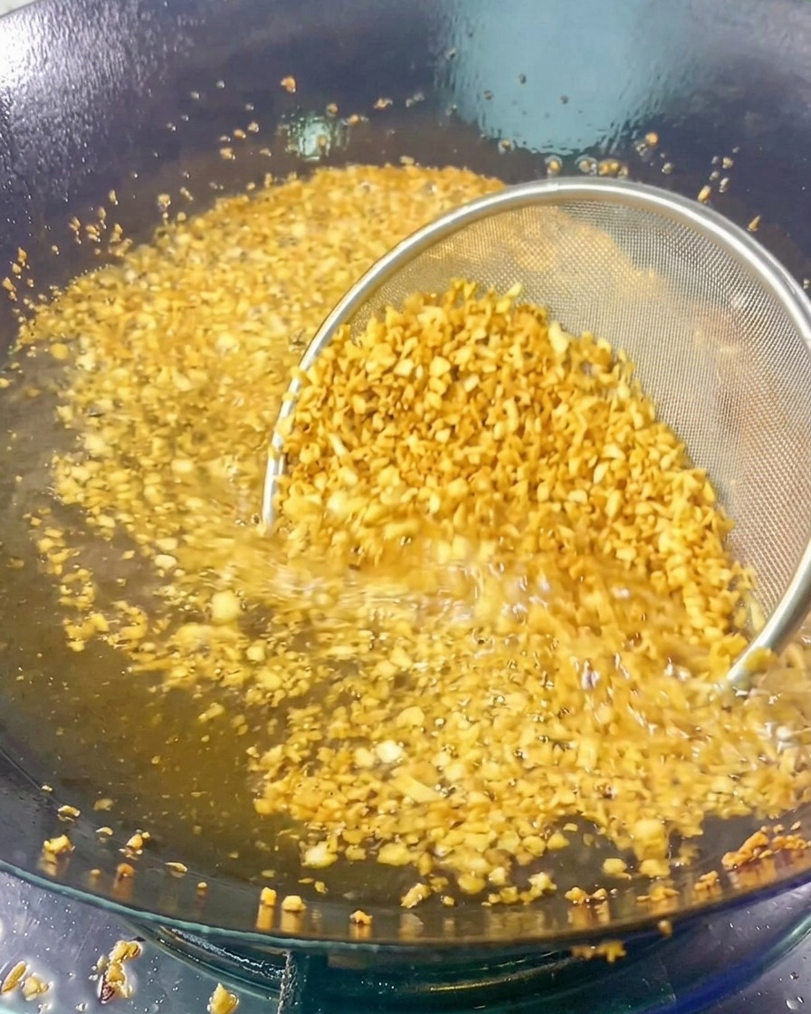 Une passoire fine remplie dail émincé plongée dans de lhuile de friture chaude pendant quil devient doré et parfumé.