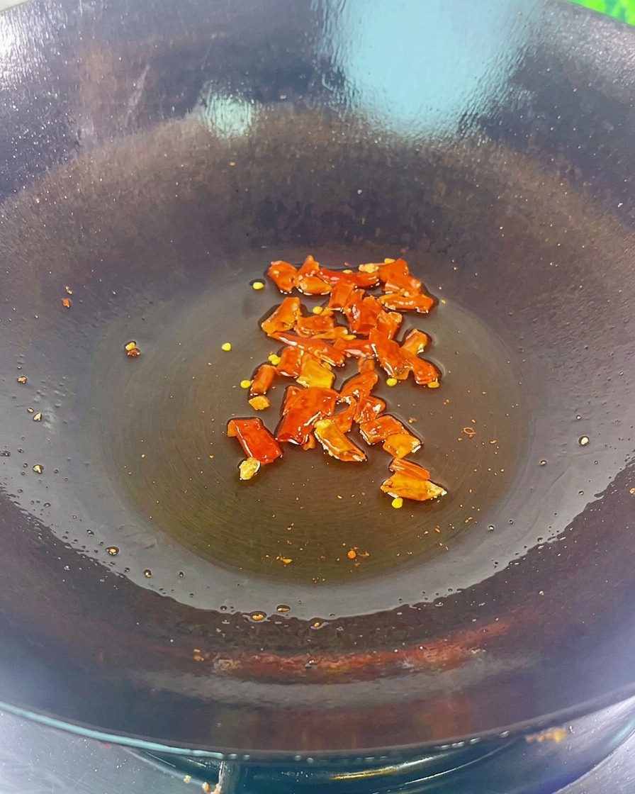 Morceaux de piment rouge séché et haricots noirs crépitant au fond dun wok sombre légèrement huilé.