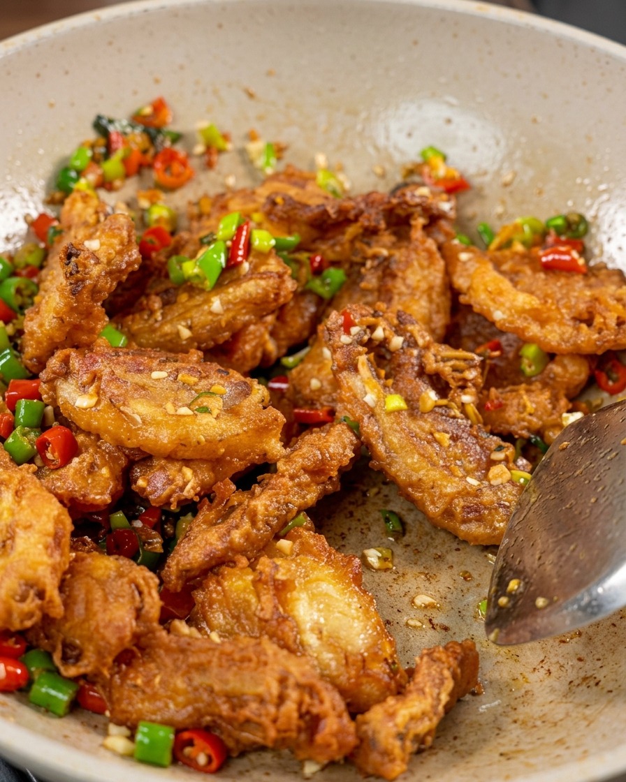 Gros plan sur la poitrine de porc croustillante, les poivrons rouges et verts et lail sautés dans un wok avec des graines de sésame blanc visibles en surface.