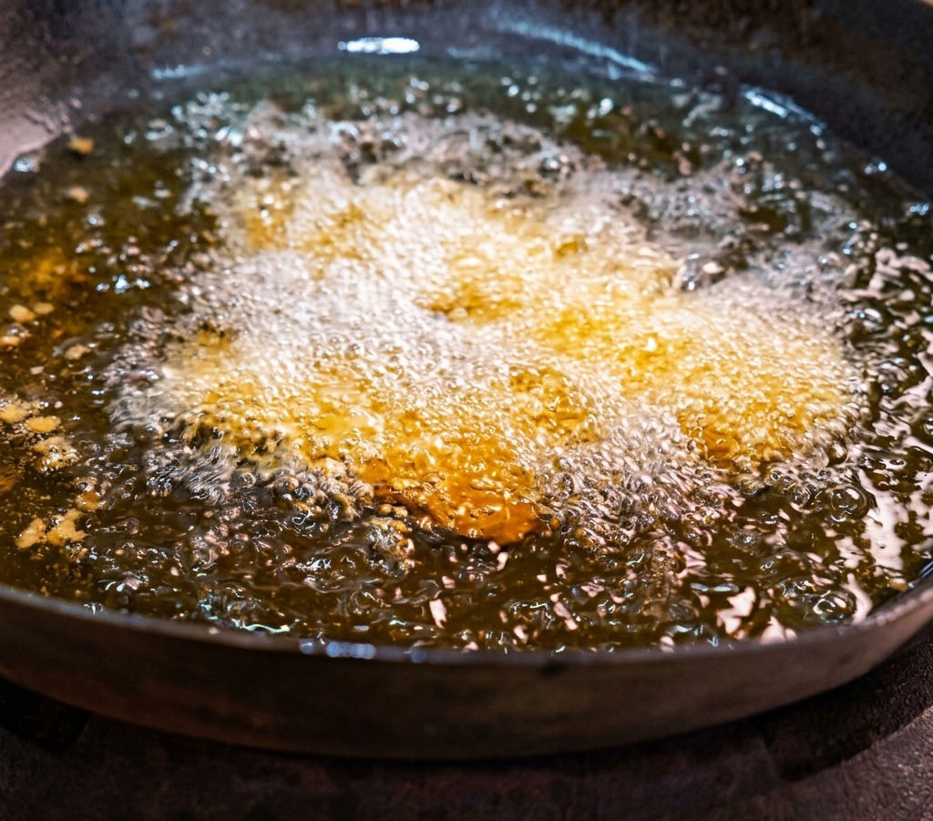 Tranches de poitrine de porc marination en train de frire dans un wok rempli dhuile chaude et bouillonnante.