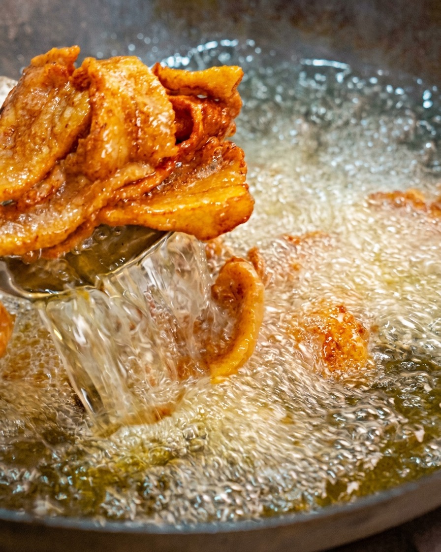 Retrait des tranches de poitrine de porc frites et dorées hors de lhuile bouillonnante à laide dune araignée de cuisine.