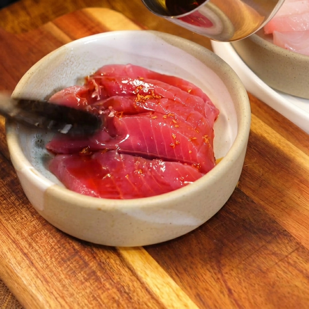 Une sauce savoureuse à base de soja versée à la cuillère sur des tranches de thon cru rouge vif dans un petit bol en céramique artisanale.