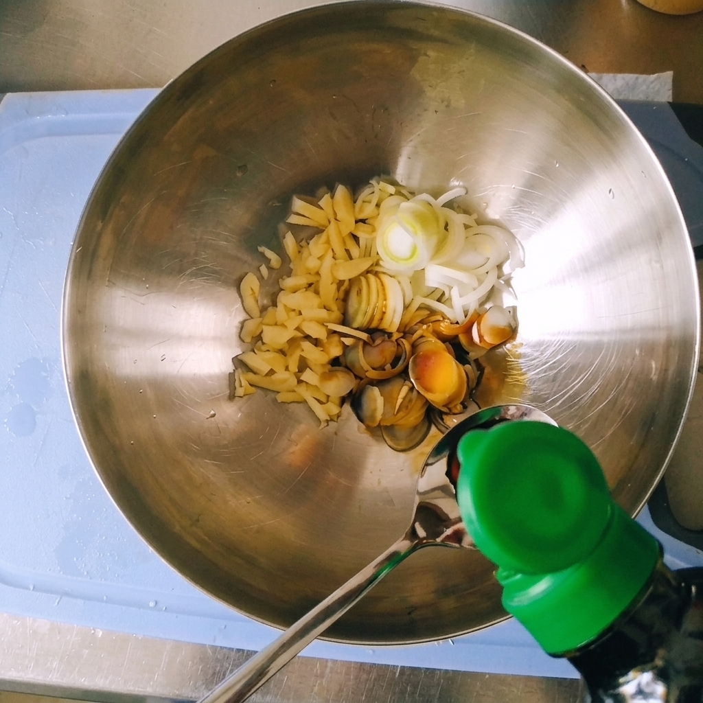 Versement de sauce soja claire dune bouteille dans une cuillère au-dessus dun bol en métal contenant des oignons verts et de lail.