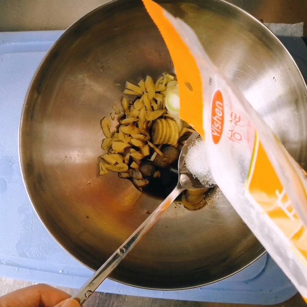 Versement de sucre blanc en poudre depuis un sachet en plastique sur une cuillère au-dessus du bol mélangeur.