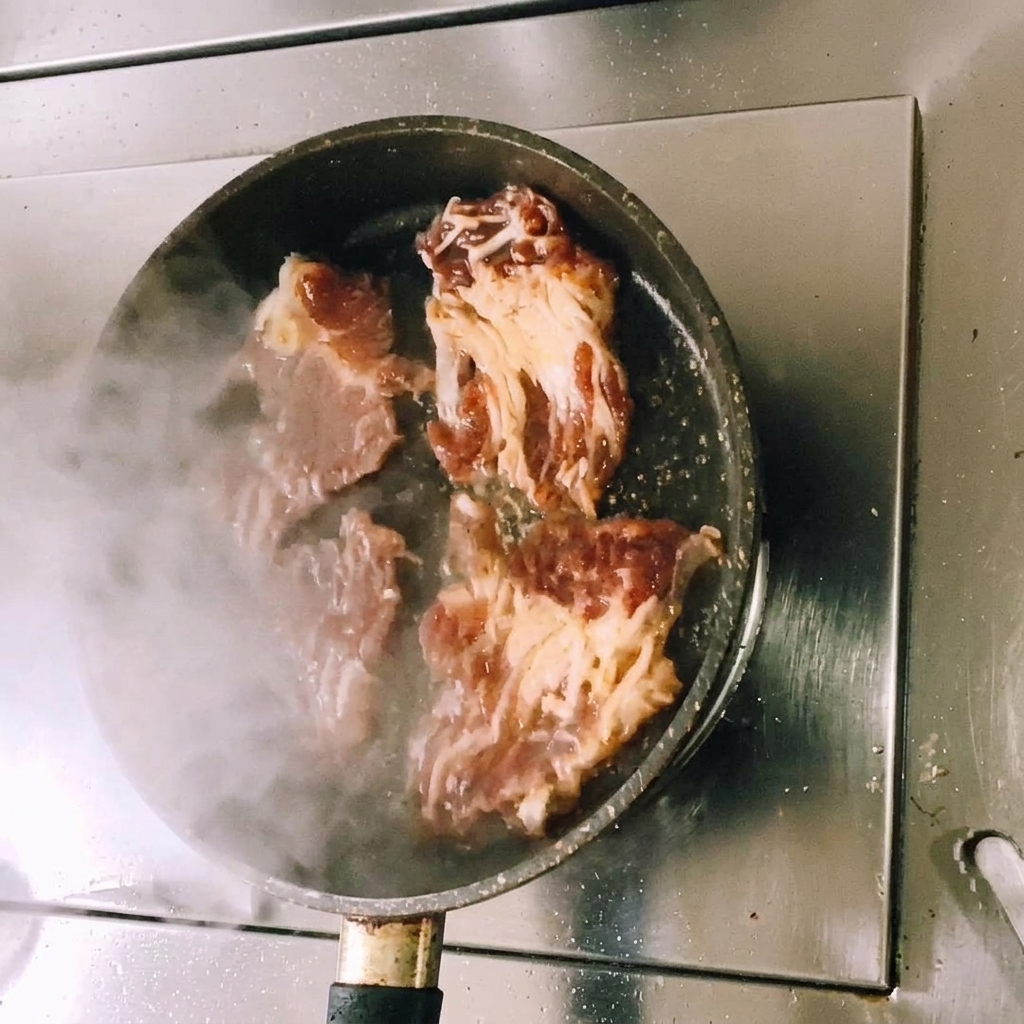 Tranches de bœuf mariné saisies dans une poêle plate avec de la vapeur visible alors que la viande commence à dorer.
