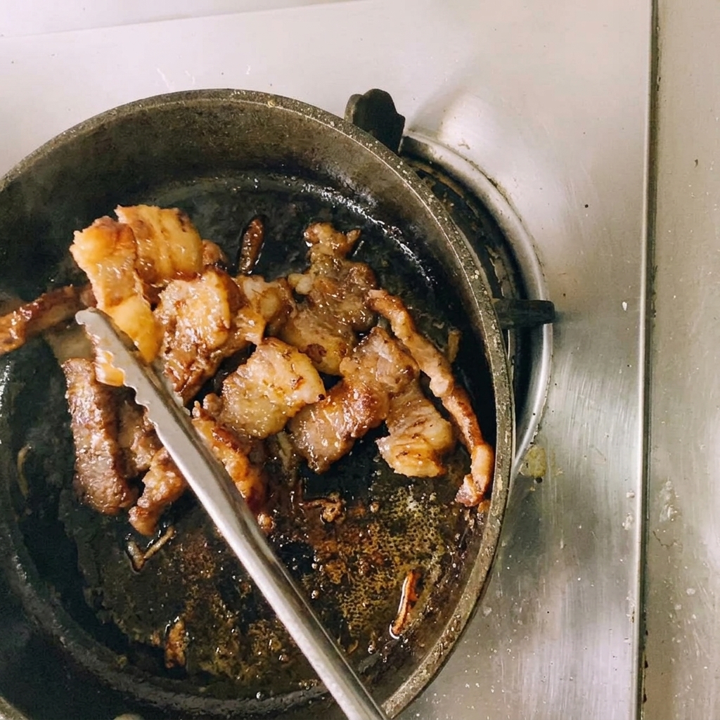 Une paire de pinces de cuisine en métal maintenant un morceau de bœuf doré pendant quil est coupé en plus petites portions au-dessus de la poêle.