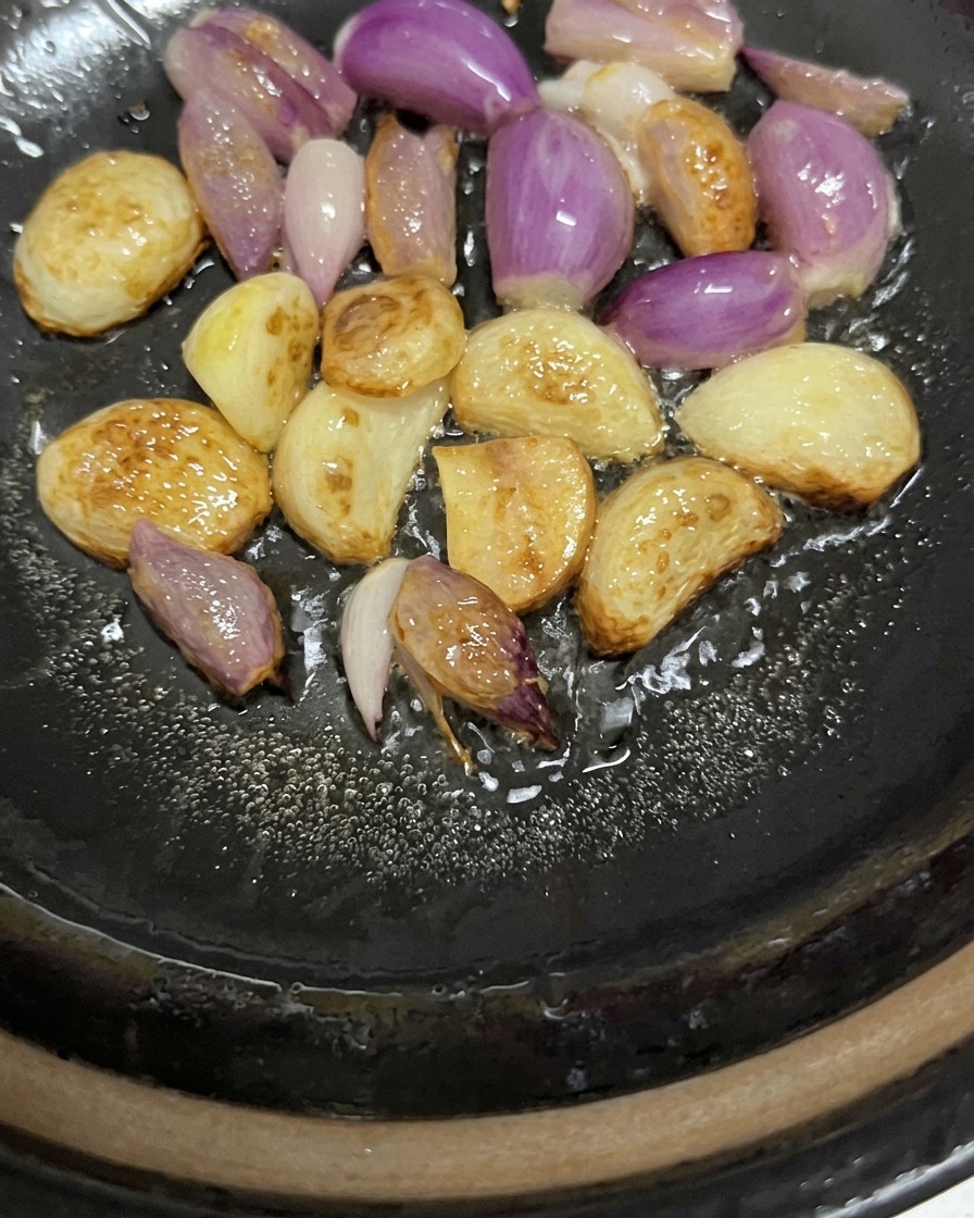 Gousses dail entières et échalotes pourpres crépitant et colorant légèrement dans lhuile au fond dune marmite.