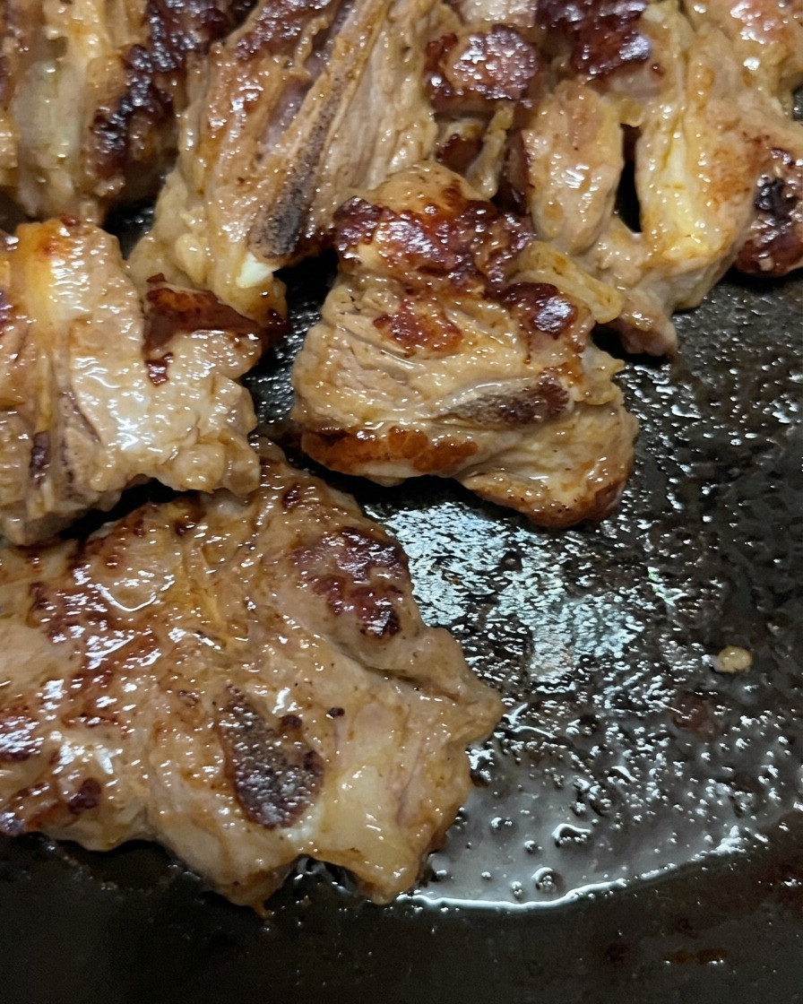 Travers de porc en train de cuire dans une poêle, retournés pour révéler une surface bien dorée et caramélisée.