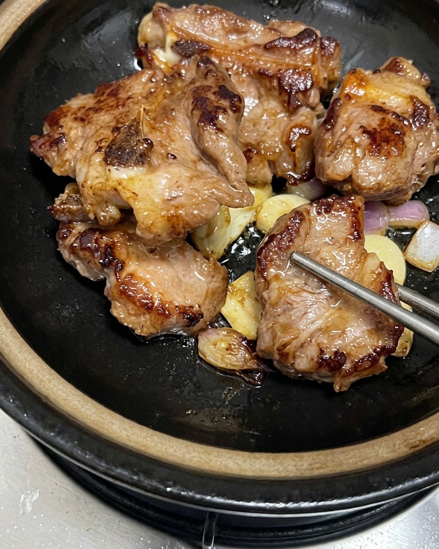 Travers de porc bien dorés disposés sur un lit dail et déchalotes revenus dans une marmite en terre noire.