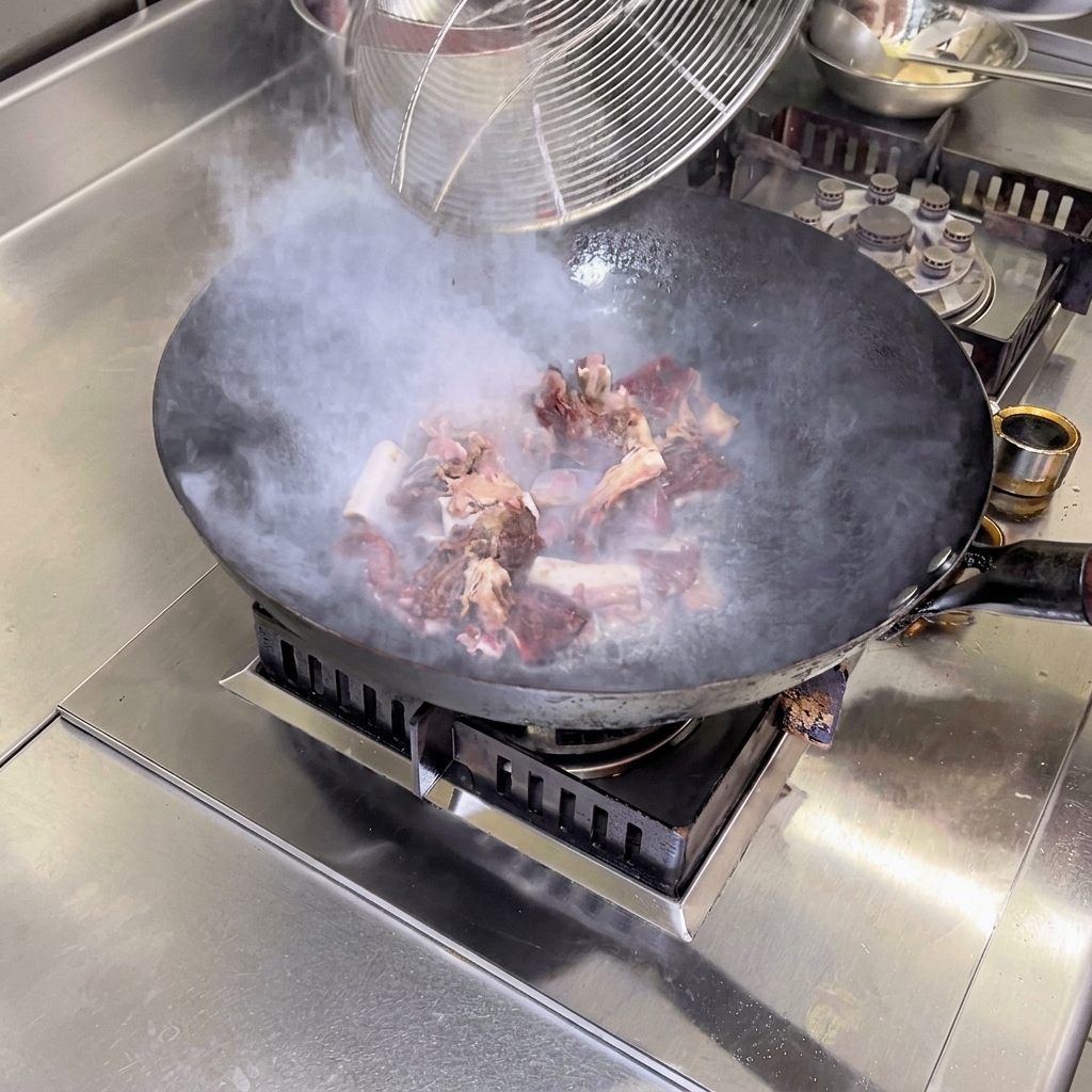 Les morceaux de porc fumé sautés à feu vif dans un wok brûlant avec de lhuile de camélia, dégageant de la vapeur.
