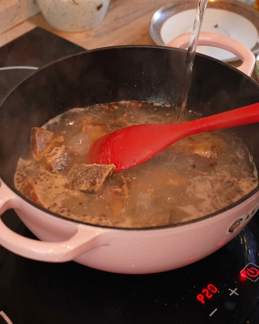 De leau chaude est versée dans une marmite contenant les travers de porc frits, le gingembre et le poivre du Sichuan.