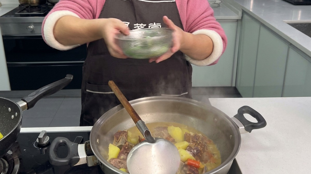 Des pousses dail vert émincées ajoutées depuis un bol transparent dans un wok fumant contenant le ragoût de porc et de pommes de terre.
