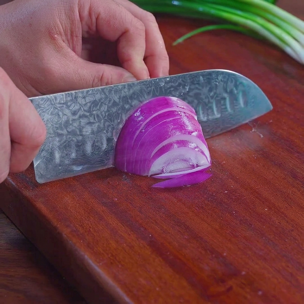 Un couteau de chef éminçant un oignon rouge en fines lamelles sur une planche à découper.
