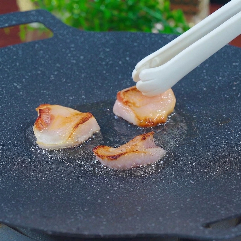 Une pince de cuisine frottant des morceaux de gras de porc sur une poêle en fonte chaude pour exprimer le saindoux.