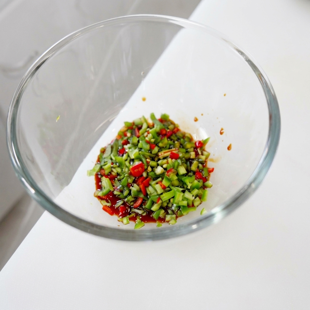 Un mélange de piments verts et rouges finement émincés et de coriandre hachée reposant dans une base liquide sombre et brillante dans un bol.