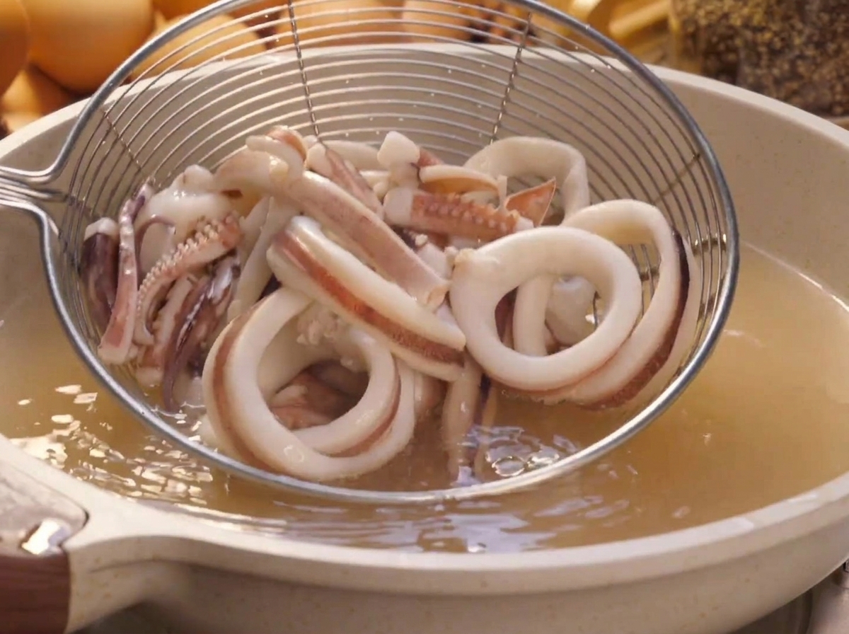 Une passoire araignée sortant les anneaux de calmar blanchis dune casserole deau bouillante.
