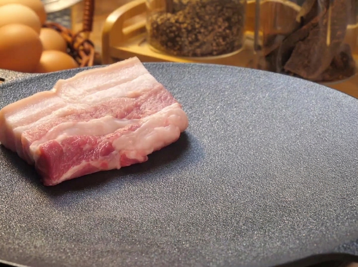Épaisses tranches de poitrine de porc crue déposées sur une plaque teppanyaki chaude et noire pour être saisies.