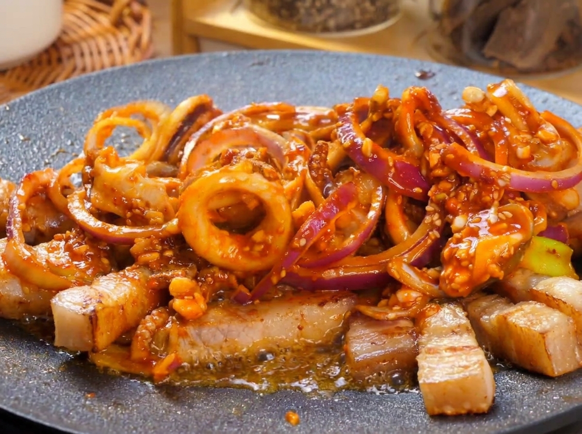 Une plaque teppanyaki chaude remplie dun sauté de poitrine de porc et de calmar à la sauce rouge épicée qui bouillonne vigoureusement, garnie de morceaux de piments verts frais.