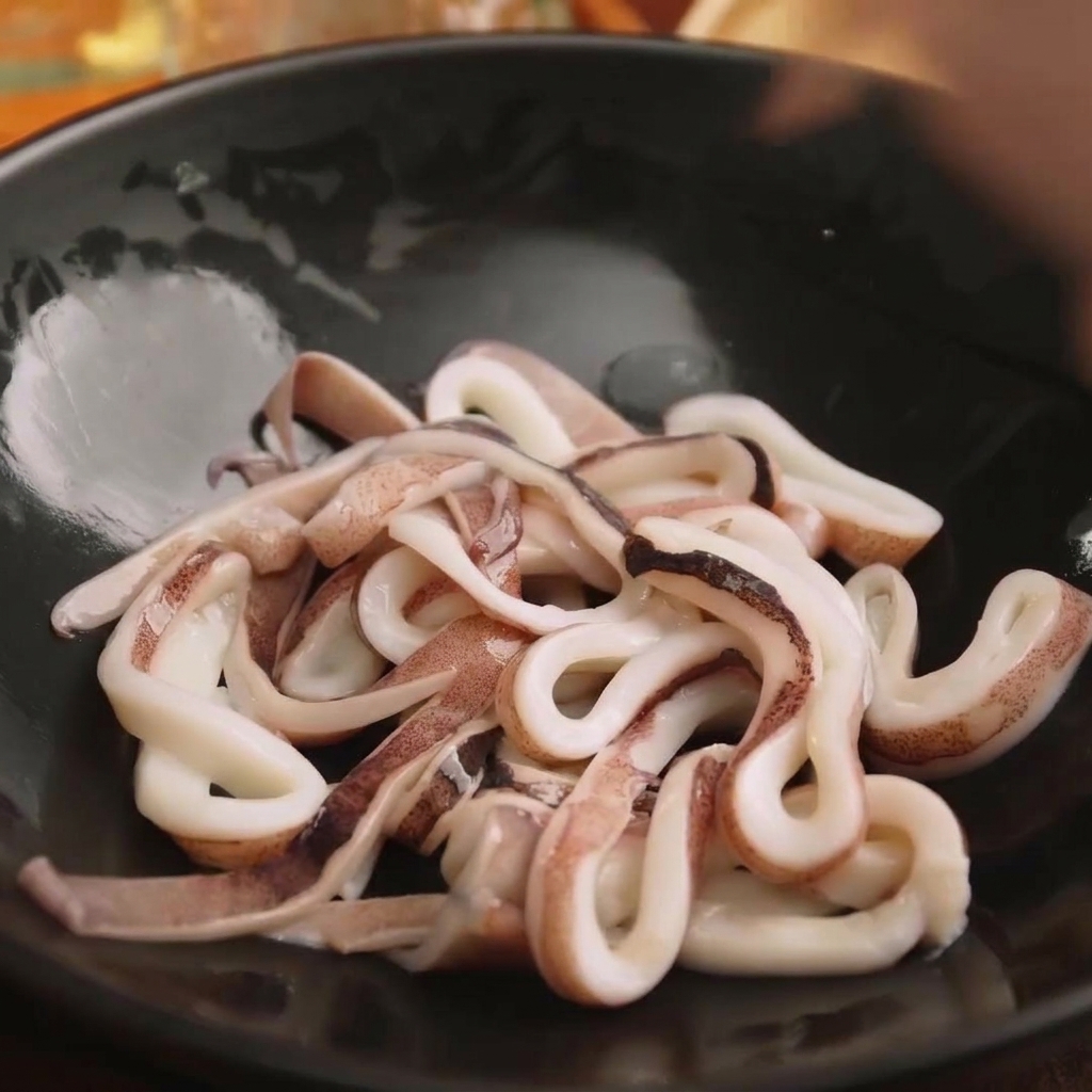 Rondelles de calamar frais dans un bol noir prêtes à être assaisonnées.