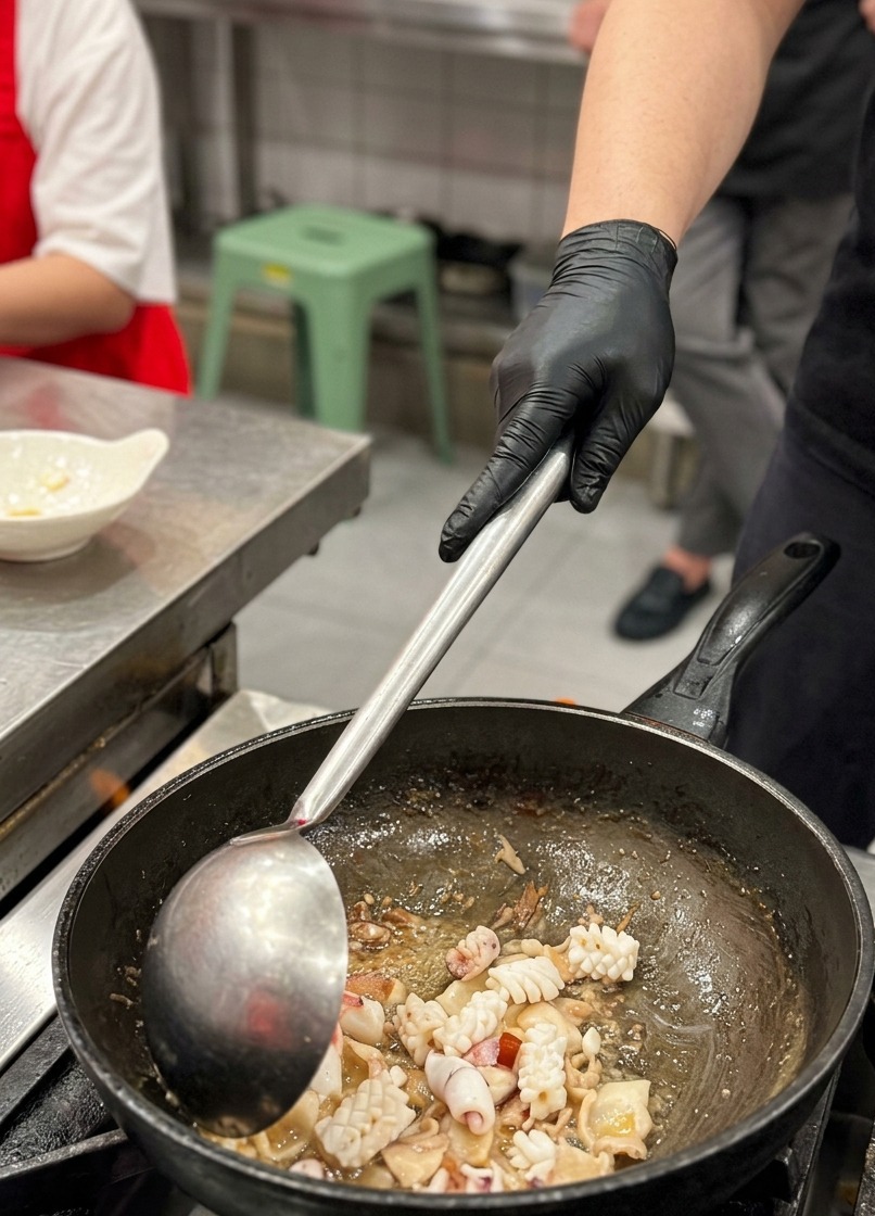 Gros plan sur les morceaux de calmar incisés mélangés aux tranches de poitrine de porc dorées dans un wok.