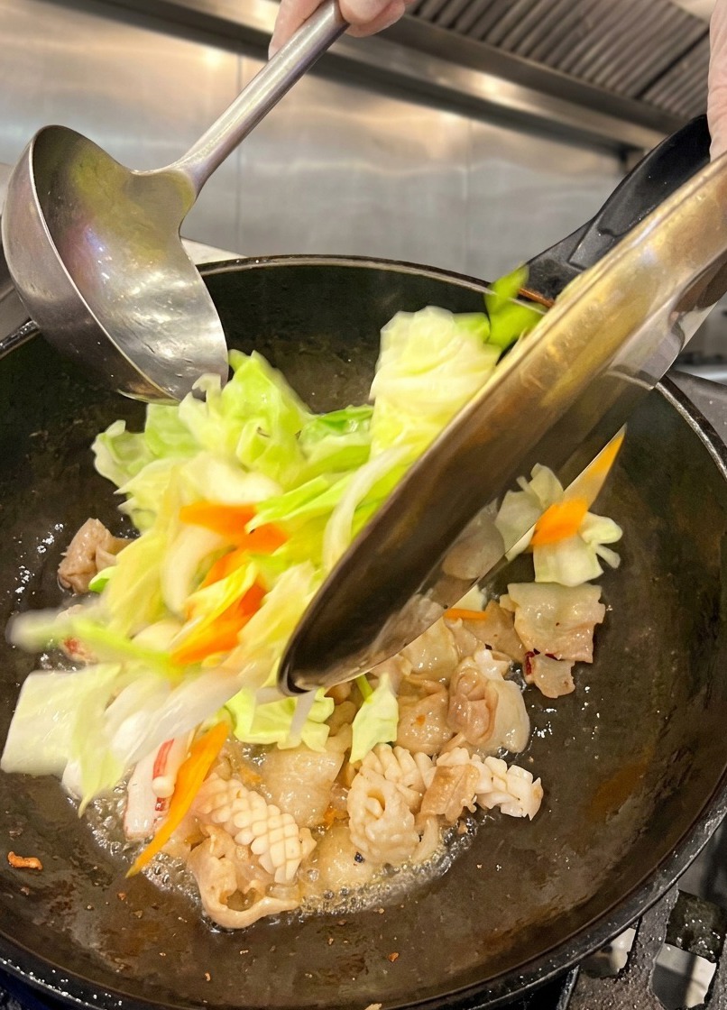 Chou vert émincé et rondelles de carottes fraîches versés depuis une assiette en métal dans un wok fumant.