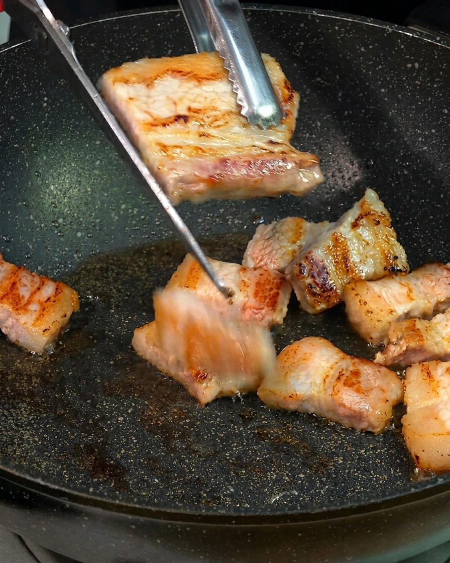 Tranches de poitrine de porc grillées coupées en petits morceaux au-dessus de la poêle avec des ciseaux de cuisine.